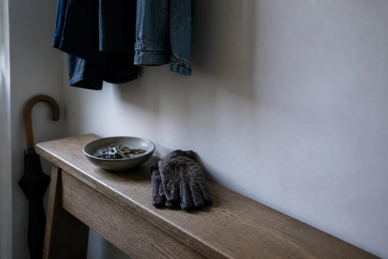 Two coats, a bowl of keys and a pair of gloves on a hallway console in early-morning light.